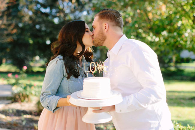 A newly engaged couple holding a cake with a sparkling LOVE topper